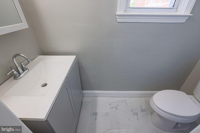 half bathroom with toilet, baseboards, marble finish floor, and vanity