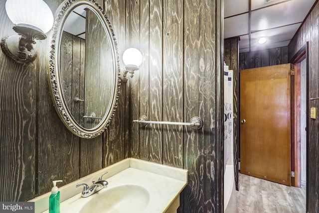 bathroom with vanity, wood walls, and wood finished floors