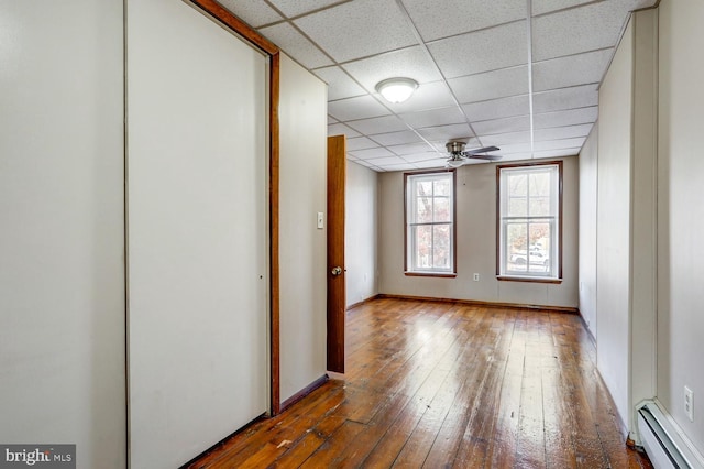 unfurnished room with baseboards, a baseboard radiator, a drop ceiling, and hardwood / wood-style flooring