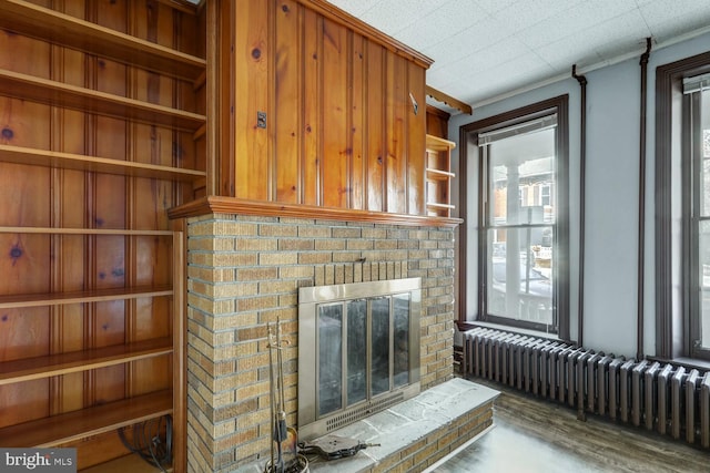 unfurnished living room with a brick fireplace, crown molding, radiator heating unit, and wood finished floors