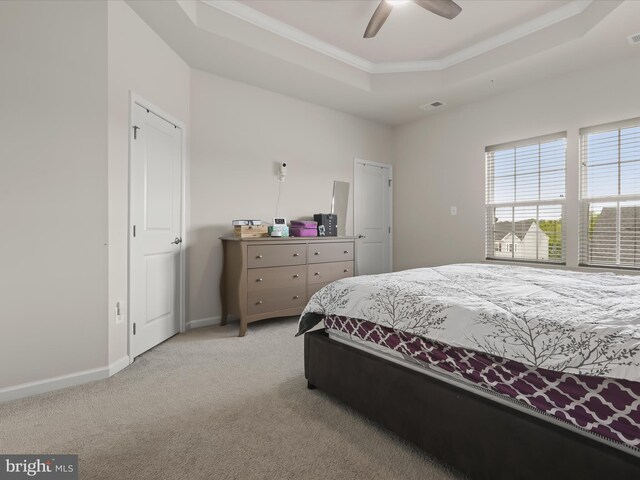 bedroom with a raised ceiling, light colored carpet, crown molding, baseboards, and a ceiling fan