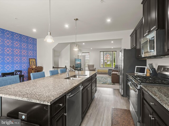 kitchen featuring appliances with stainless steel finishes, wallpapered walls, a sink, open floor plan, and an accent wall