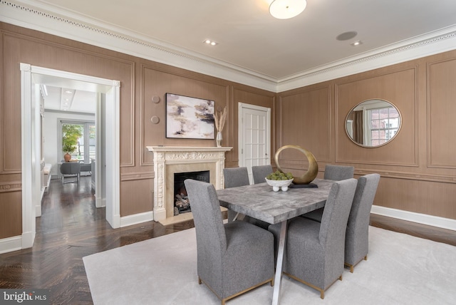 dining space with crown molding, baseboards, a fireplace, and a decorative wall