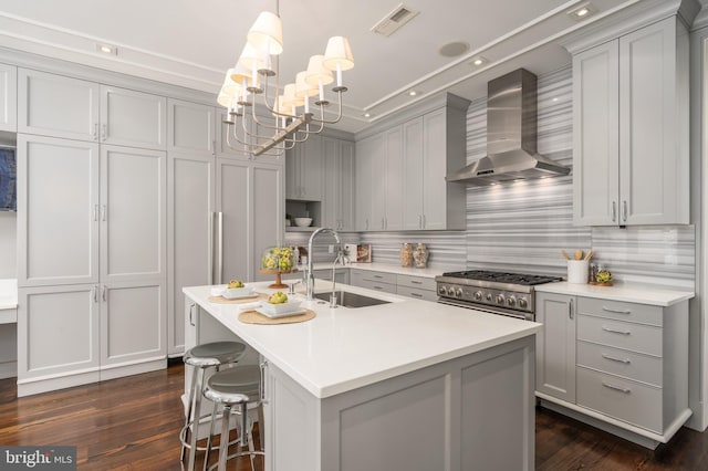 kitchen featuring wall chimney range hood, a notable chandelier, a sink, visible vents, and gray cabinetry