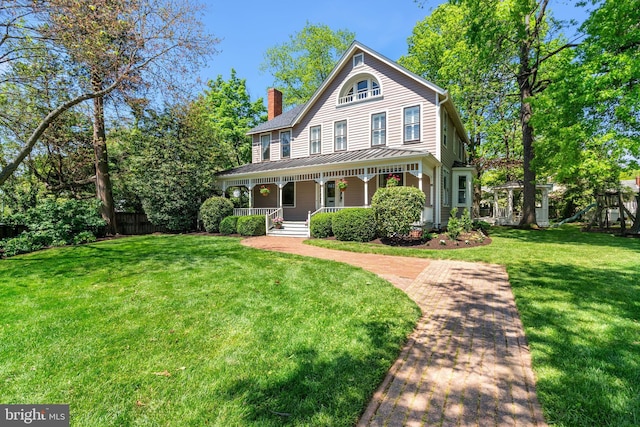 view of front of home featuring a porch, a front yard, a chimney, a standing seam roof, and metal roof