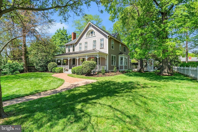rear view of house with covered porch, a yard, fence, and a chimney