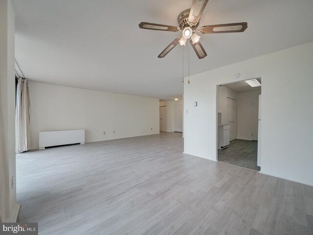 unfurnished living room with a ceiling fan, radiator, and wood finished floors