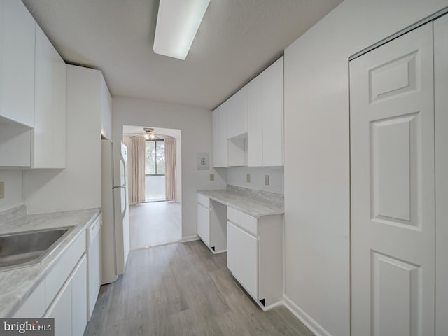 kitchen featuring white cabinets, a sink, light wood finished floors, light countertops, and freestanding refrigerator