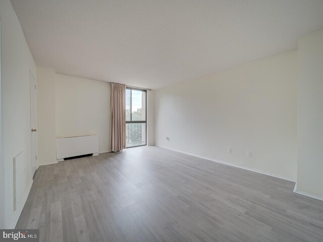 empty room featuring baseboards, radiator, wood finished floors, and a wall of windows