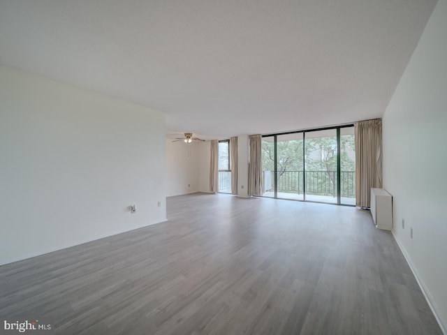 spare room featuring a wall of windows, ceiling fan, and wood finished floors
