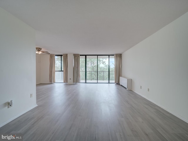 unfurnished room with a wall of windows, baseboards, a ceiling fan, and wood finished floors