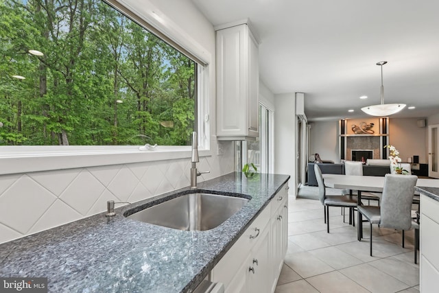 kitchen with a sink, tasteful backsplash, white cabinetry, light tile patterned floors, and decorative light fixtures