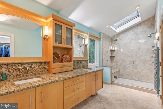 bathroom featuring a stall shower, a skylight, double vanity, backsplash, and vaulted ceiling
