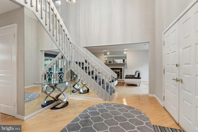 entryway with stairs, wood finished floors, a fireplace, baseboards, and a towering ceiling