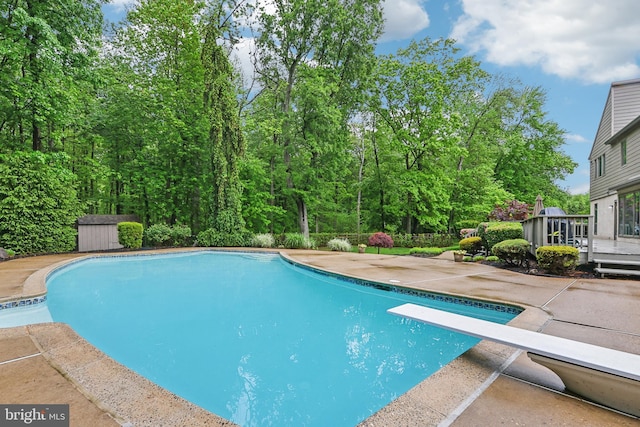 outdoor pool with a diving board, a wooden deck, and a patio area