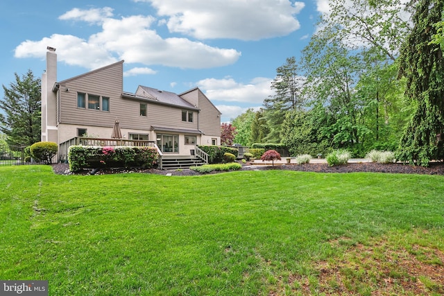 rear view of house with a chimney, a yard, and a wooden deck