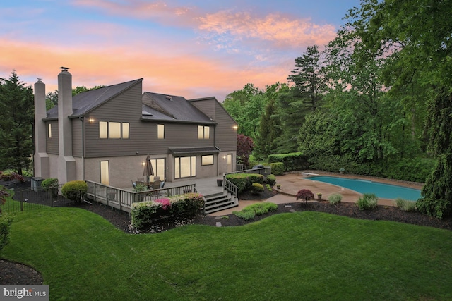 rear view of house with a deck, an outdoor pool, a chimney, roof with shingles, and stucco siding