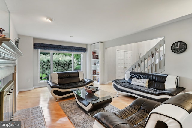living area featuring stairway, wood finished floors, a fireplace with flush hearth, and baseboards