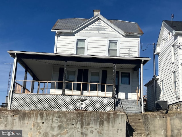 view of front facade featuring covered porch, a chimney, and metal roof