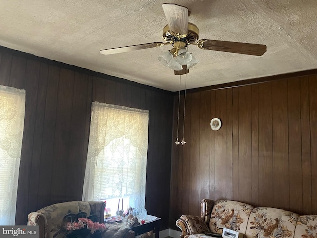 living area with wooden walls, a ceiling fan, and a textured ceiling