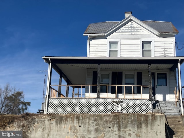 view of front of property with a porch, a chimney, and metal roof
