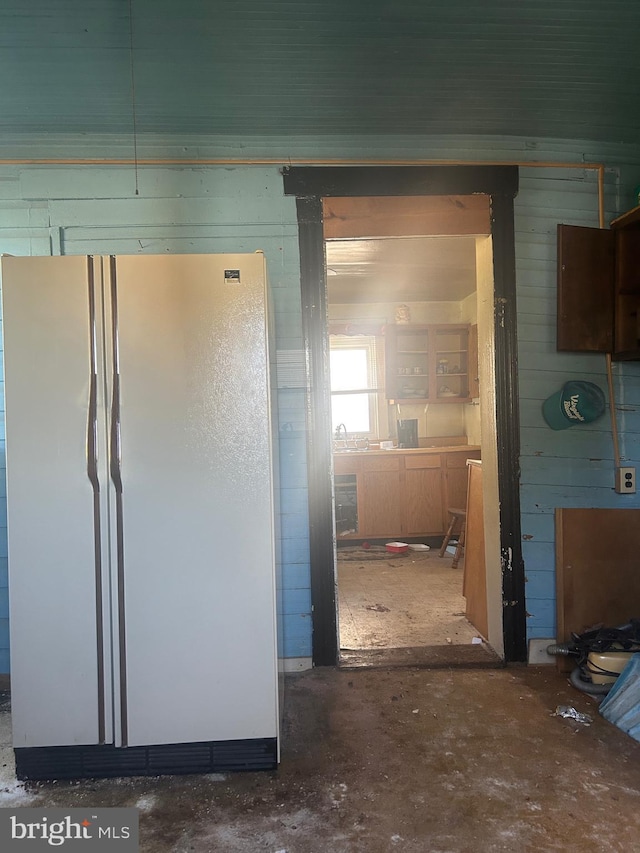 interior space featuring freestanding refrigerator, wood walls, and unfinished concrete floors