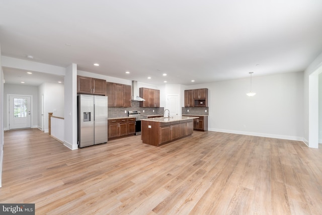 kitchen with backsplash, appliances with stainless steel finishes, a sink, open floor plan, and wall chimney exhaust hood