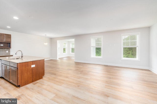 kitchen featuring light stone countertops, a sink, light wood finished floors, baseboards, and open floor plan