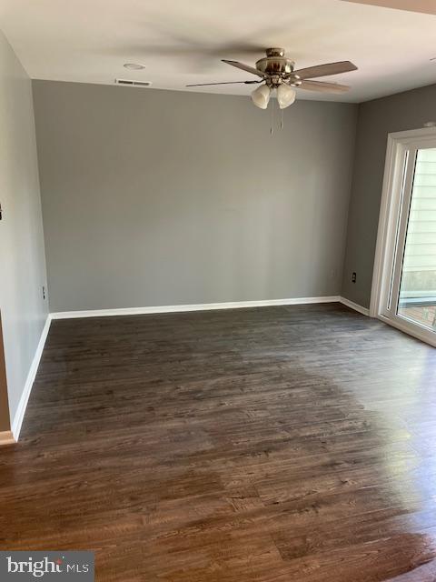 unfurnished room with dark wood-style flooring, a ceiling fan, baseboards, and visible vents