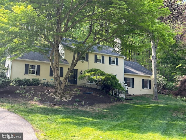 tri-level home with roof with shingles, stucco siding, and a front yard
