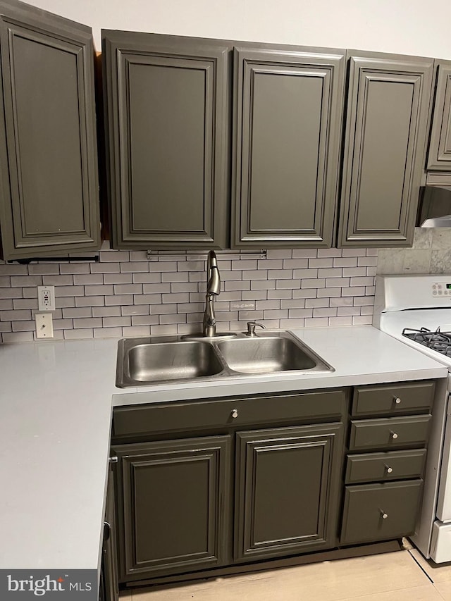 kitchen featuring gas stove, a sink, backsplash, and light countertops