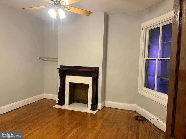 unfurnished living room with a ceiling fan, a fireplace, wood finished floors, and baseboards