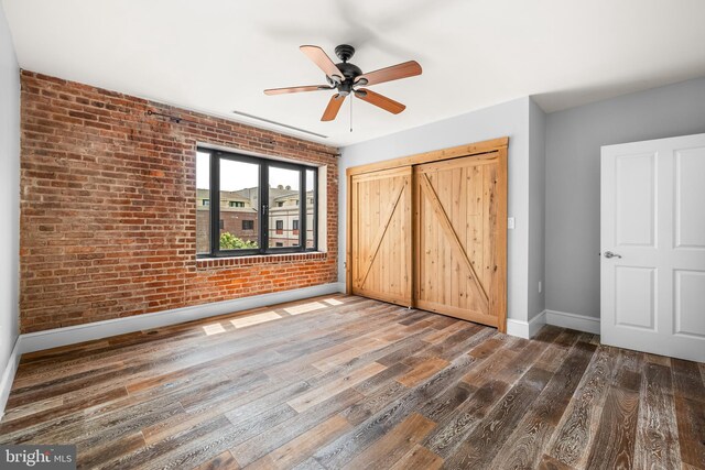1000 Fell St Unit 633, Baltimore, MD 21231 - unfurnished bedroom featuring brick wall, baseboards, wood finished floors, a closet, and ceiling fan