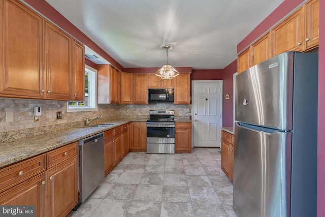 kitchen featuring brown cabinetry, backsplash, light stone countertops, a sink, and stainless steel appliances