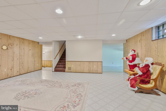 finished basement with visible vents, wood walls, stairway, a paneled ceiling, and tile patterned floors