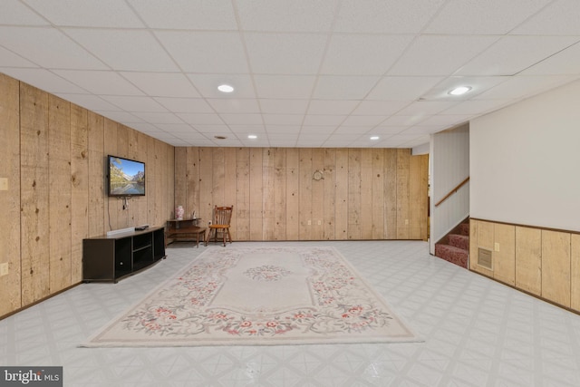 sitting room featuring visible vents, stairway, wooden walls, light floors, and a drop ceiling