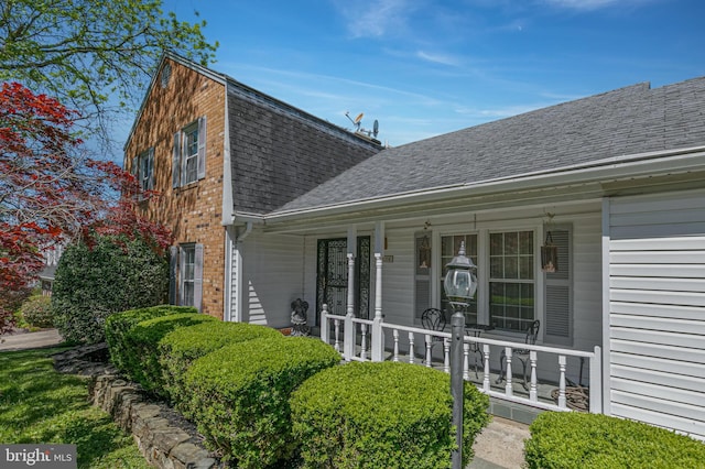 entrance to property featuring brick siding, roof with shingles, and covered porch