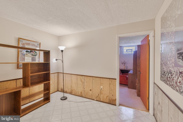 empty room with a textured ceiling, tile patterned floors, and a wainscoted wall