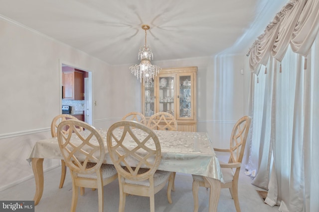 carpeted dining room featuring an inviting chandelier, baseboards, and crown molding