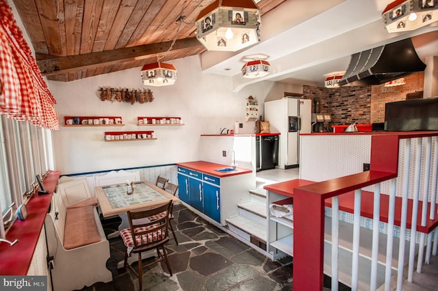 interior space featuring ventilation hood, white fridge with ice dispenser, vaulted ceiling with beams, wood ceiling, and blue cabinets