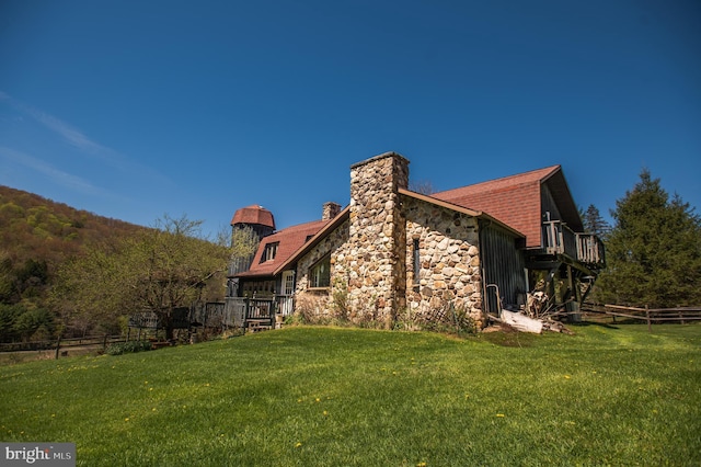 back of house with a lawn, a chimney, fence, and stone siding
