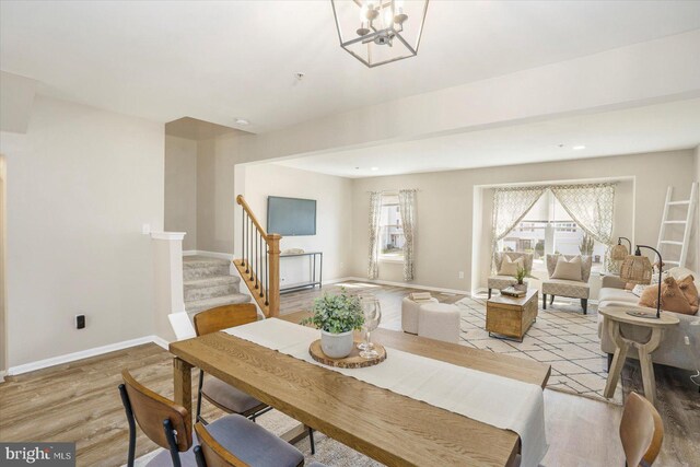 dining room featuring baseboards, a notable chandelier, stairway, and light wood-type flooring