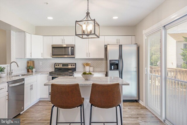 kitchen with backsplash, a sink, light wood-style floors, stainless steel appliances, and white cabinetry