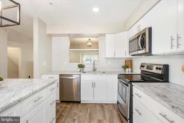 kitchen featuring backsplash, light wood-type flooring, a sink, stainless steel appliances, and white cabinetry