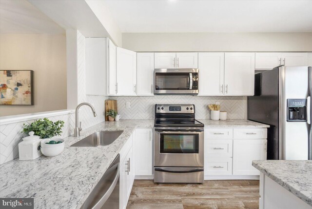 kitchen with a sink, light stone counters, light wood-style floors, stainless steel appliances, and white cabinetry
