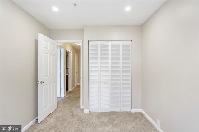 unfurnished bedroom with recessed lighting, baseboards, light carpet, and a closet