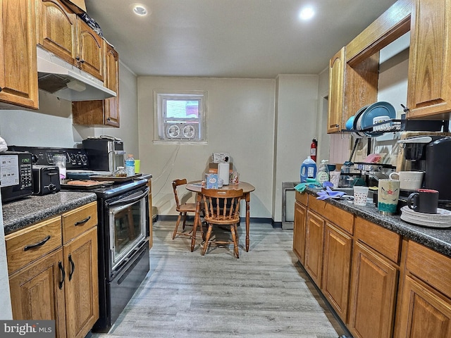 kitchen featuring dark countertops, brown cabinetry, black appliances, and under cabinet range hood