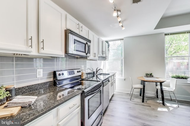 kitchen with white cabinets, appliances with stainless steel finishes, a sink, light wood finished floors, and backsplash