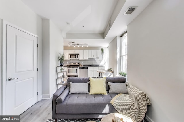 living area featuring light wood-style floors, track lighting, baseboards, and visible vents