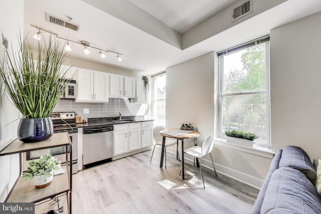 kitchen featuring dark countertops, a sink, stainless steel appliances, white cabinetry, and visible vents